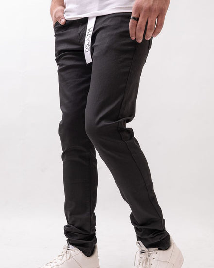 Person wearing black pants with a brand logo and white sneakers on a light gray background