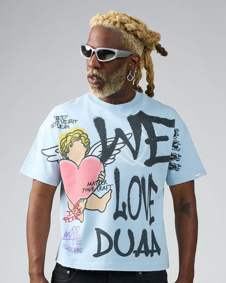 Person wearing a light blue t-shirt with graphic designs and text, standing against a plain background.