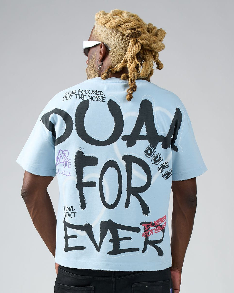 Person wearing a light blue t-shirt with black text on the back, standing against a plain background.