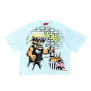 A light blue short-sleeve graphic t-shirt featuring a cartoon skull wearing sunglasses and a black tank top, holding a bottle in front of a brick wall graphic with the word 'WAR' in yellow.
