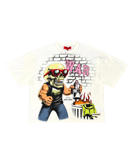 A white short-sleeve graphic t-shirt featuring a cartoon illustration of a skull in a yellow helmet and red sunglasses, holding a gun next to a burning car, with the word 'WAR' in pink graffiti-style letters on a brick wall background.