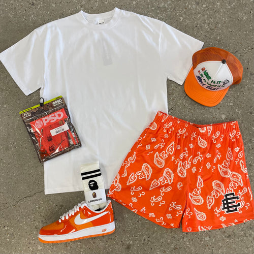 WHITE TEE WITH ORANGE SHORTS WITH ORANGE AND WHITE SHOES SURROUNDED WITH ACCESSORIES. 