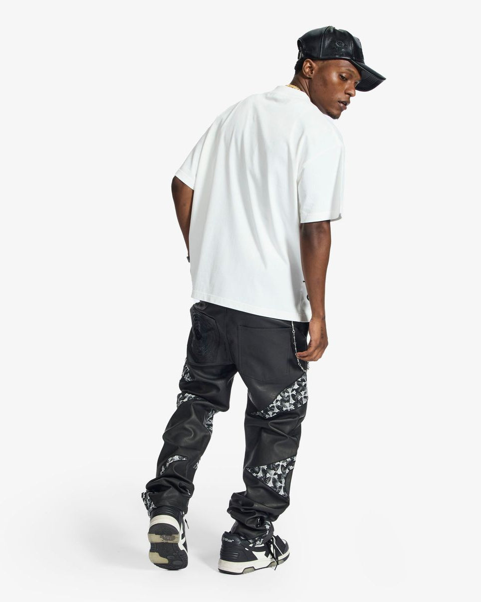 Person wearing a white t-shirt, black pants with floral patterns, and a black cap on a white background