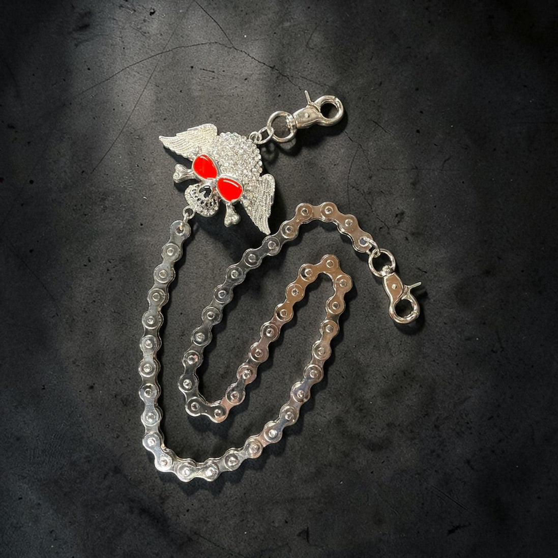 Silver chain with a decorative clasp on a dark textured surface. A WINGED SKULL AS THE MAIN DESIGN.