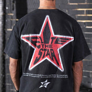 Person wearing a black t-shirt with a red star design on the back, standing against a brick wall.