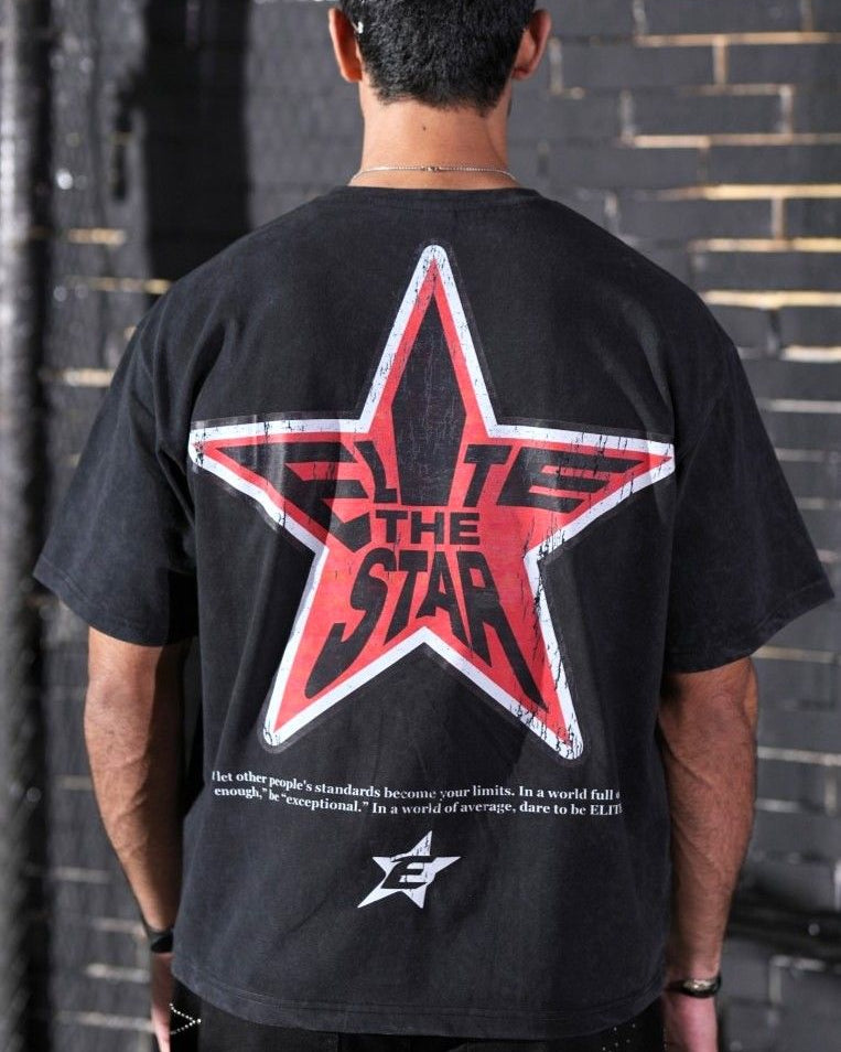 Person wearing a black t-shirt with a red star design on the back, standing against a brick wall.