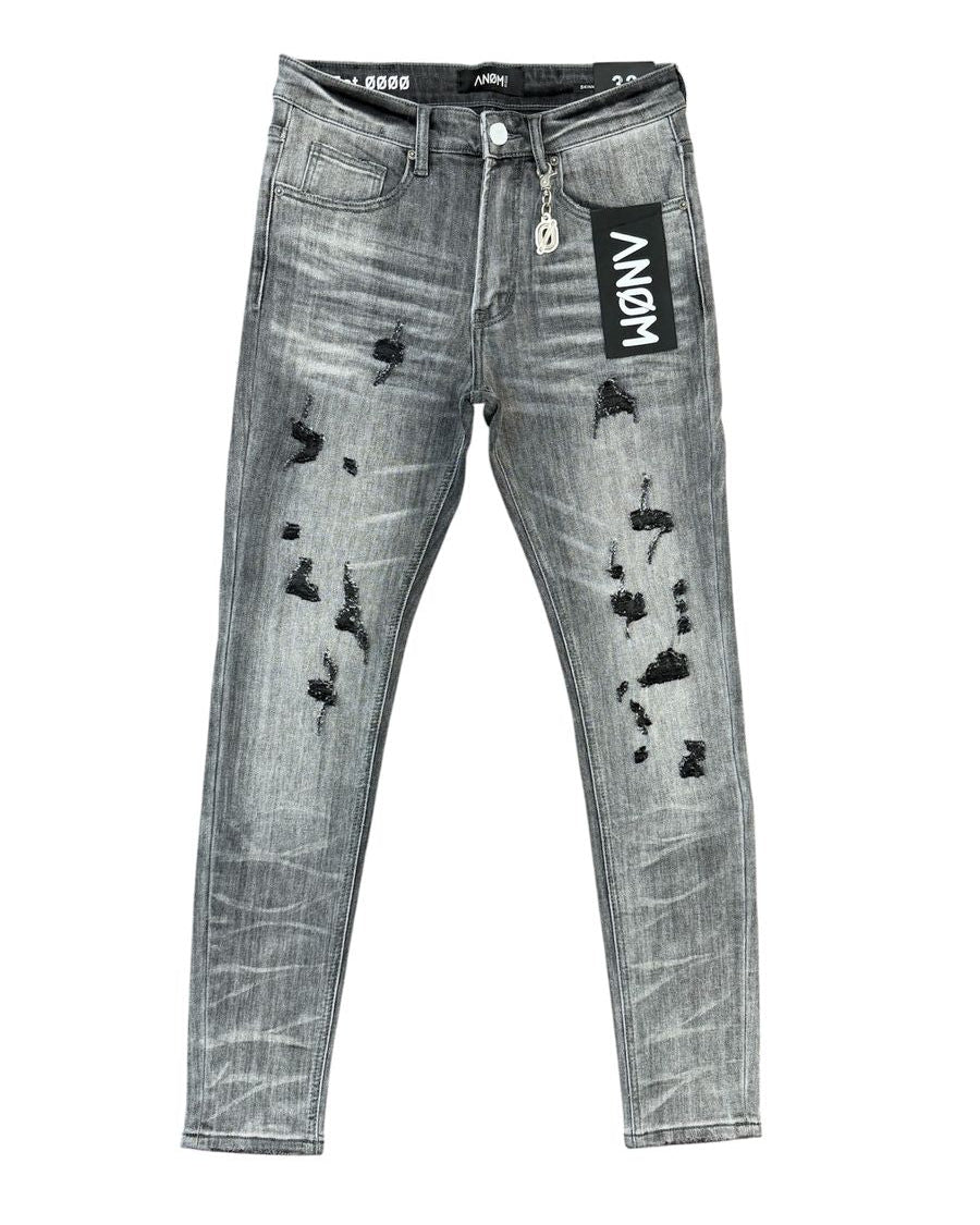 Distressed gray denim jeans with black ripped details, featuring a black hangtag with 'ANOM' on the pocket and a black inner waistband.