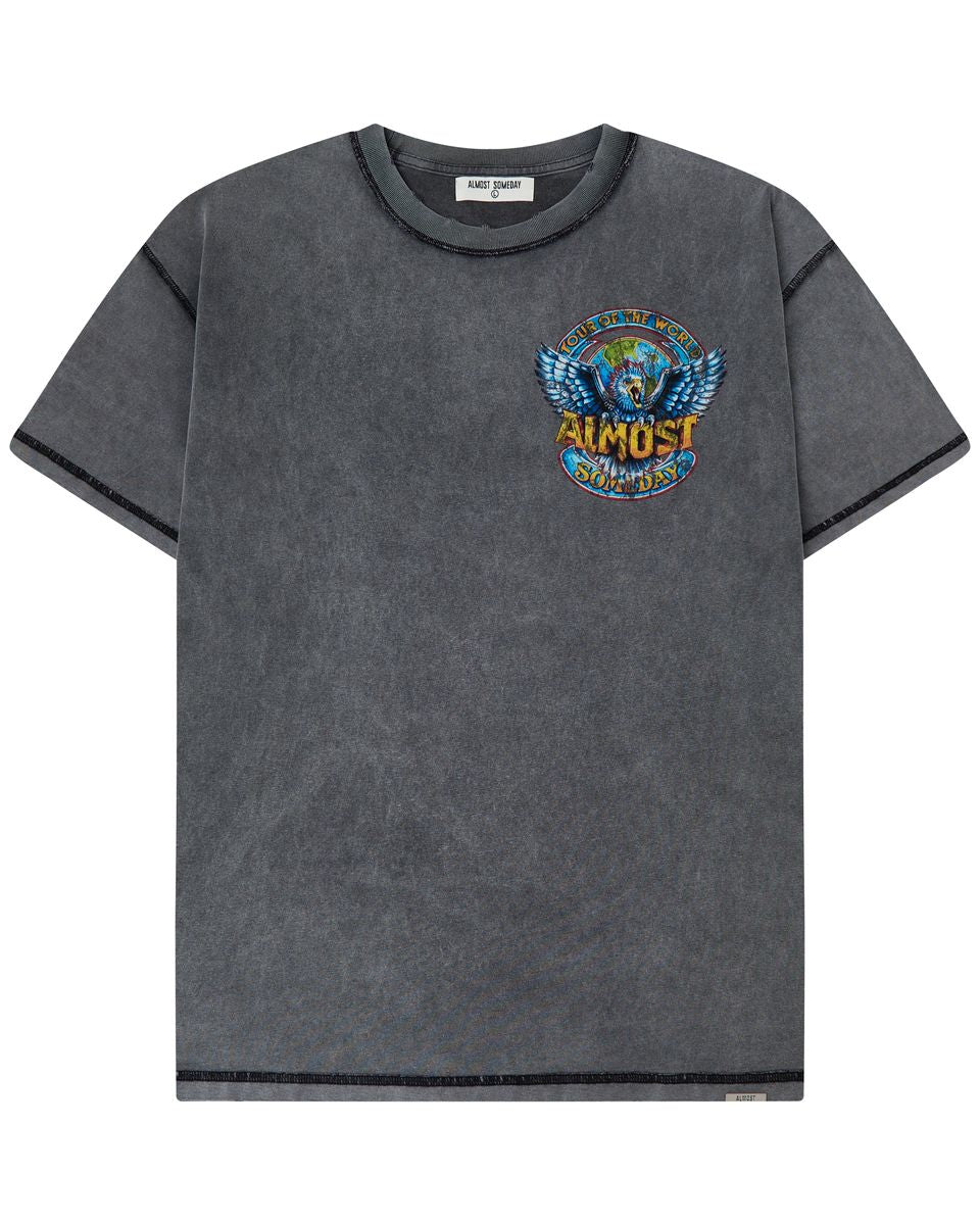A dark gray mineral-wash short-sleeve t-shirt with a colorful graphic on the left chest featuring a winged globe and the text 'TOUR OF THE WORLD ALMOST SOMEDAY'.