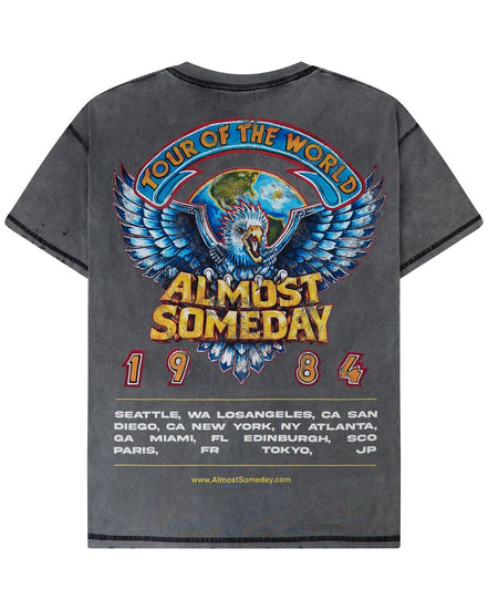 A dark gray washed graphic t-shirt shown from the back, featuring a large colorful print of an eagle and globe with the text 'TOUR OF THE WORLD ALMOST SOMEDAY 1984' and a list of tour cities.