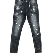 Distressed black denim jeans with white 'ANOM' lettering on the right thigh, ripped details, and a silver metal zipper pull, shown flat against a white background.
