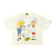 An off-white short-sleeve graphic t-shirt featuring a cartoon illustration of two characters, a skull, and the text 'KILL YOUR DEMONS' on the front, displayed flat against a white background.