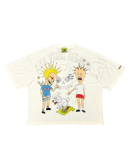An off-white short-sleeve graphic t-shirt featuring a cartoon illustration of two characters, a skull, and the text 'KILL YOUR DEMONS' on the front, displayed flat against a white background.