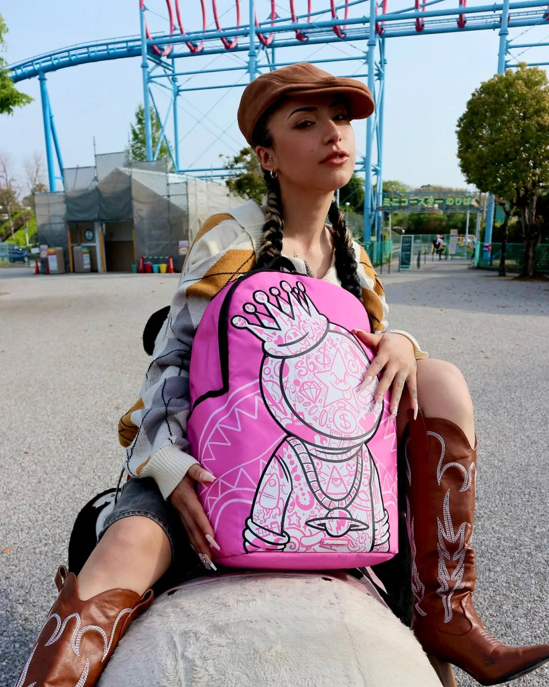 Person holding a pink backpack with a design, sitting on a bench in an outdoor setting.