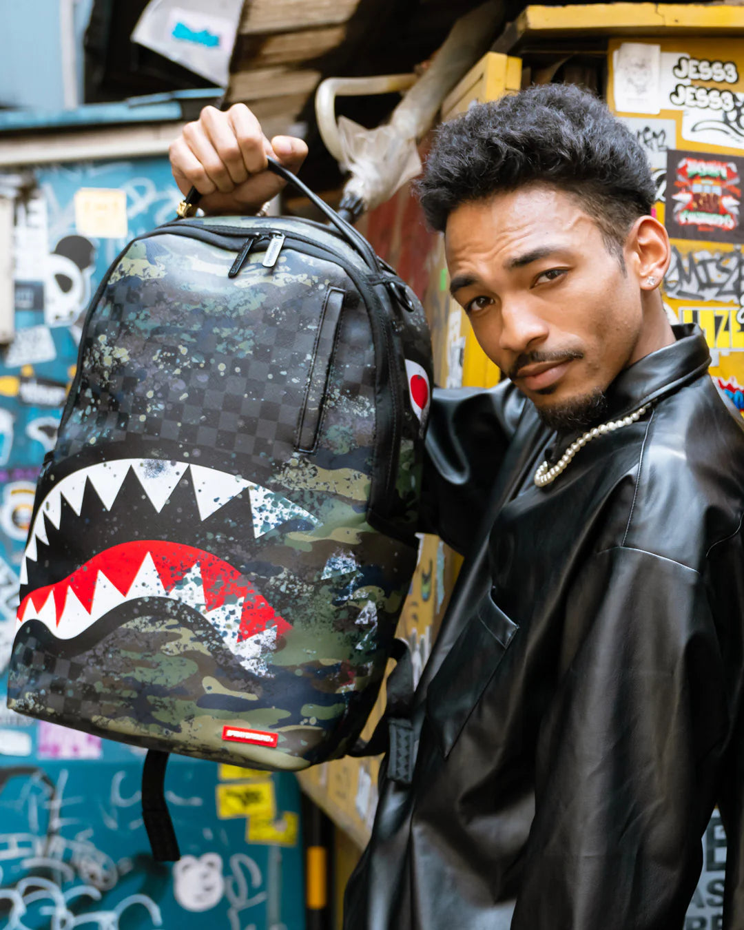 Person holding a camouflage backpack with a shark mouth design in an urban setting.