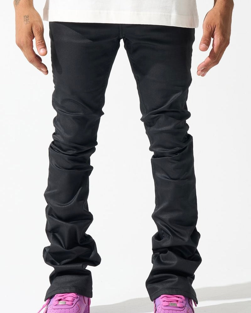 A person standing wearing black waxed stacked jeans and pink sneakers.