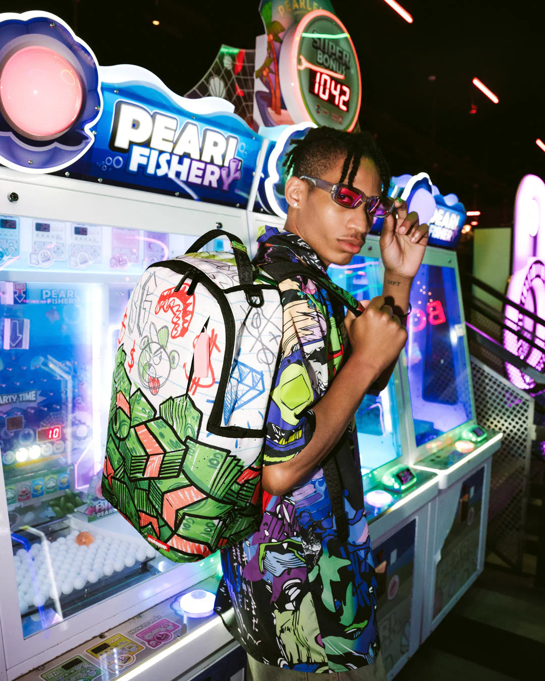 Person wearing a colorful outfit and backpack in front of an arcade machine with 'Pearl Fisher' branding.
