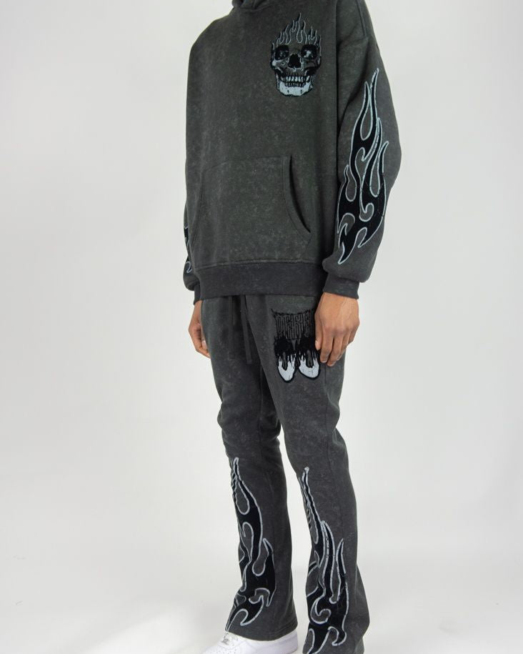 Person wearing a dark gray hoodie and pants with skull designs on a white background