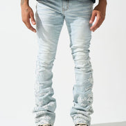 A pair of light-wash, stacked jeans featuring intricate floral lace appliques along the legs.