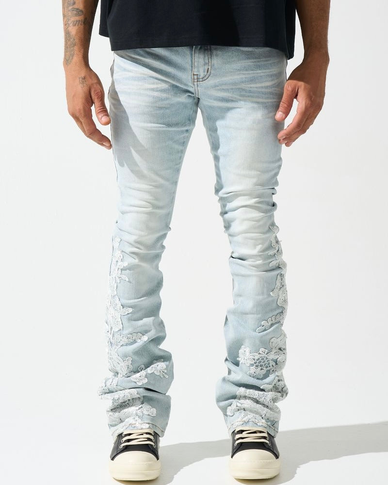 A pair of light-wash, stacked jeans featuring intricate floral lace appliques along the legs.