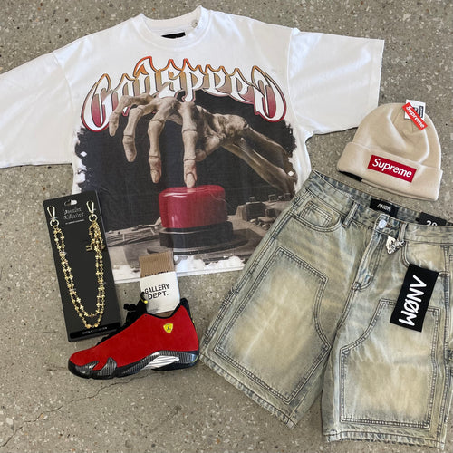 Collection of fashion items including a graphic t-shirt, sneakers, beanie, and denim shorts on a concrete surface.