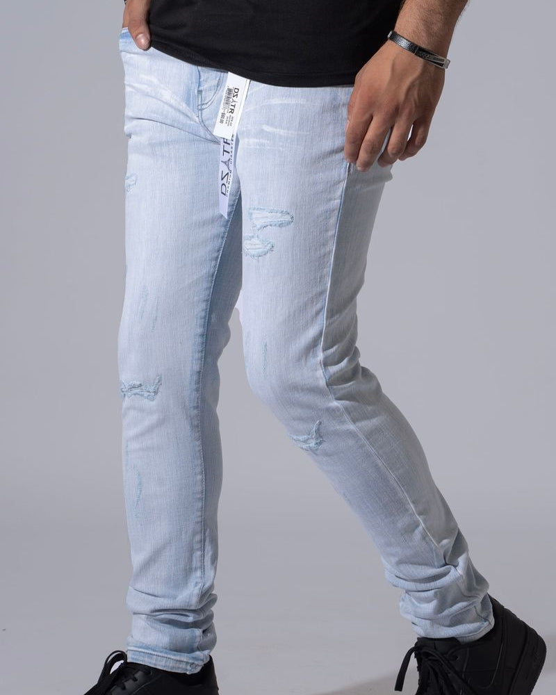 Light wash distressed denim jeans worn by a model, paired with a black t-shirt and black sneakers, shown from the waist down against a neutral gray background.
