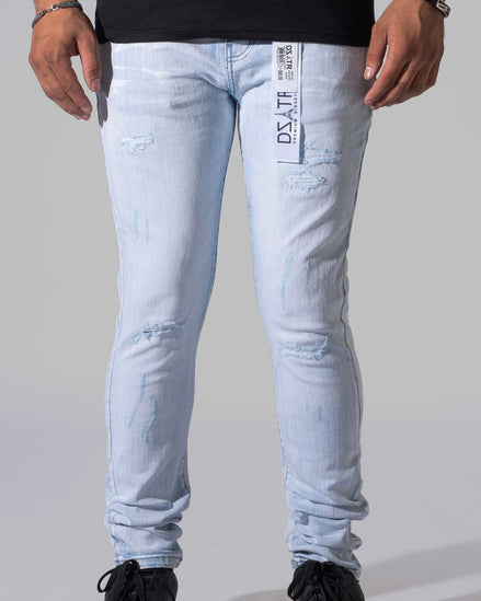 Light-wash distressed skinny jeans with a visible brand tag on the pocket, modeled with black sneakers against a neutral gray background.