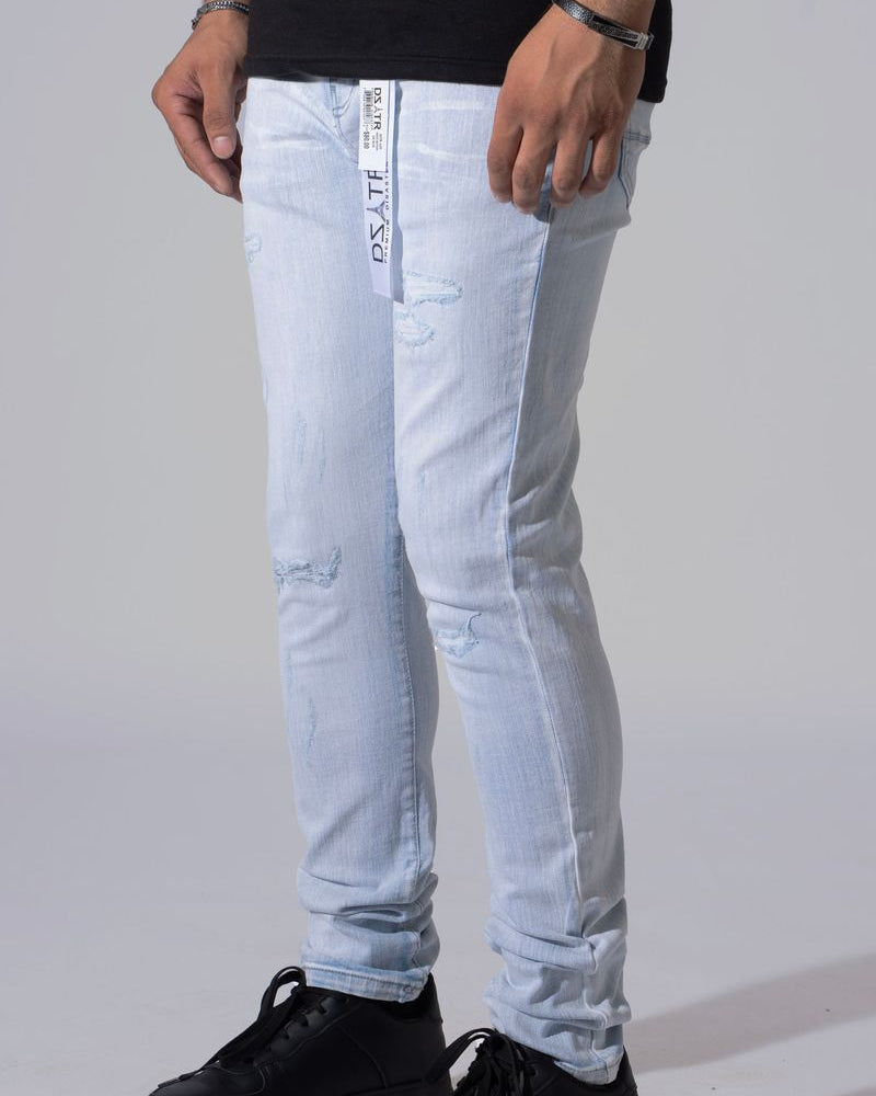 Light wash blue slim-fit jeans with distressed details and a white vertical brand tag on the pocket, worn by a model with black sneakers against a light gray background.
