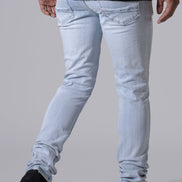 Light wash slim-fit jeans worn by a model, shown from the back as they are paired with a black t-shirt and black sneakers against a solid gray background.