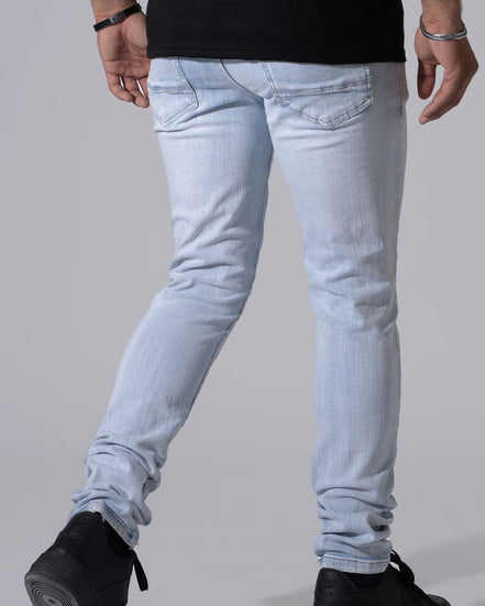 Light wash slim-fit jeans worn by a model, shown from the back as they are paired with a black t-shirt and black sneakers against a solid gray background.