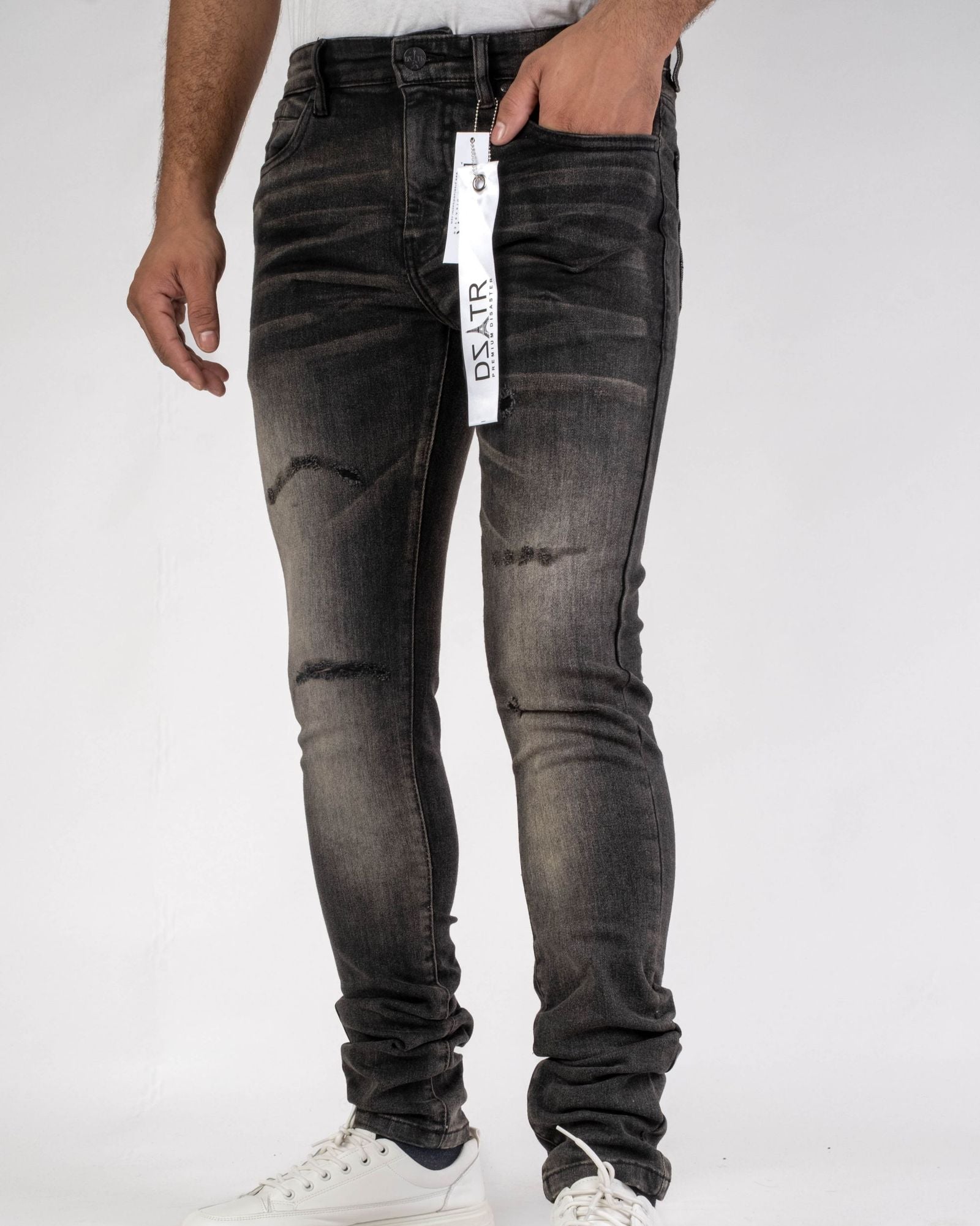 Person wearing black distressed jeans with a brand tag on a white background