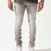 A person standing against a white background, wearing gray skinny jeans with subtle distressing on the knees and white sneakers.