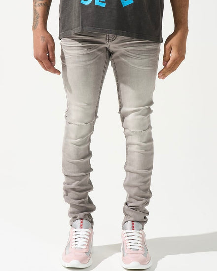 A person standing against a white background, wearing gray skinny jeans with subtle distressing on the knees and white sneakers.