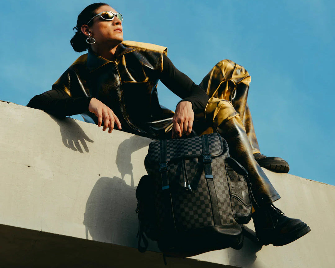 Person in stylish outfit with backpack against a blue sky