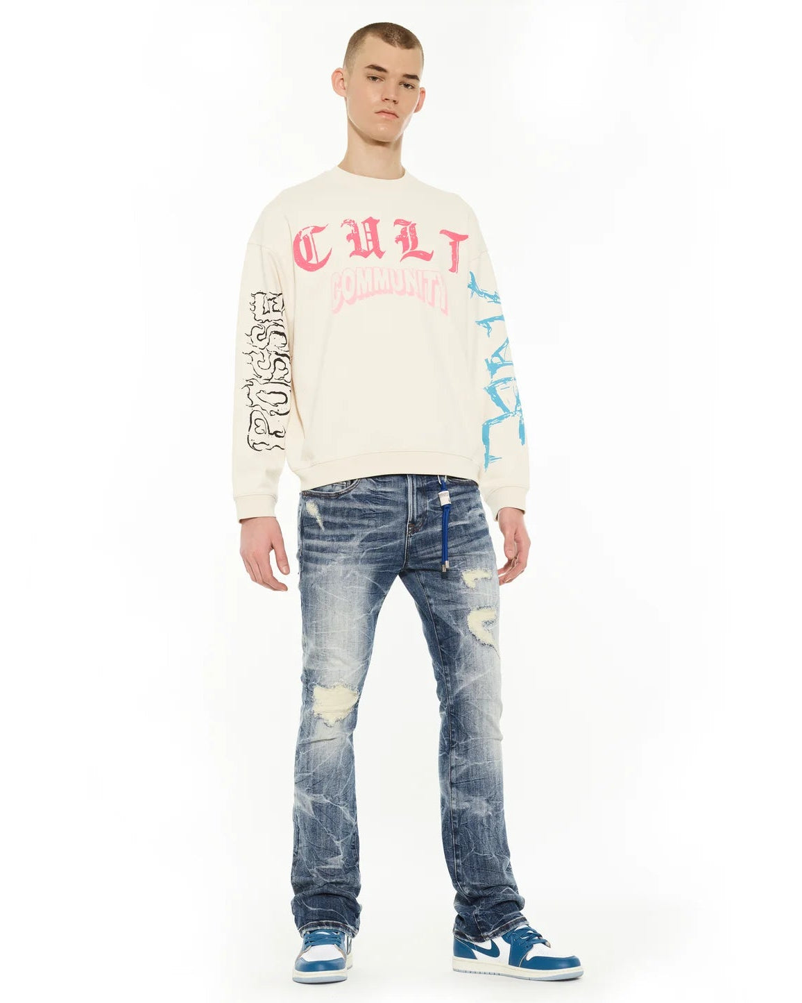 Person wearing a cream sweatshirt with colorful text and blue jeans on a white background