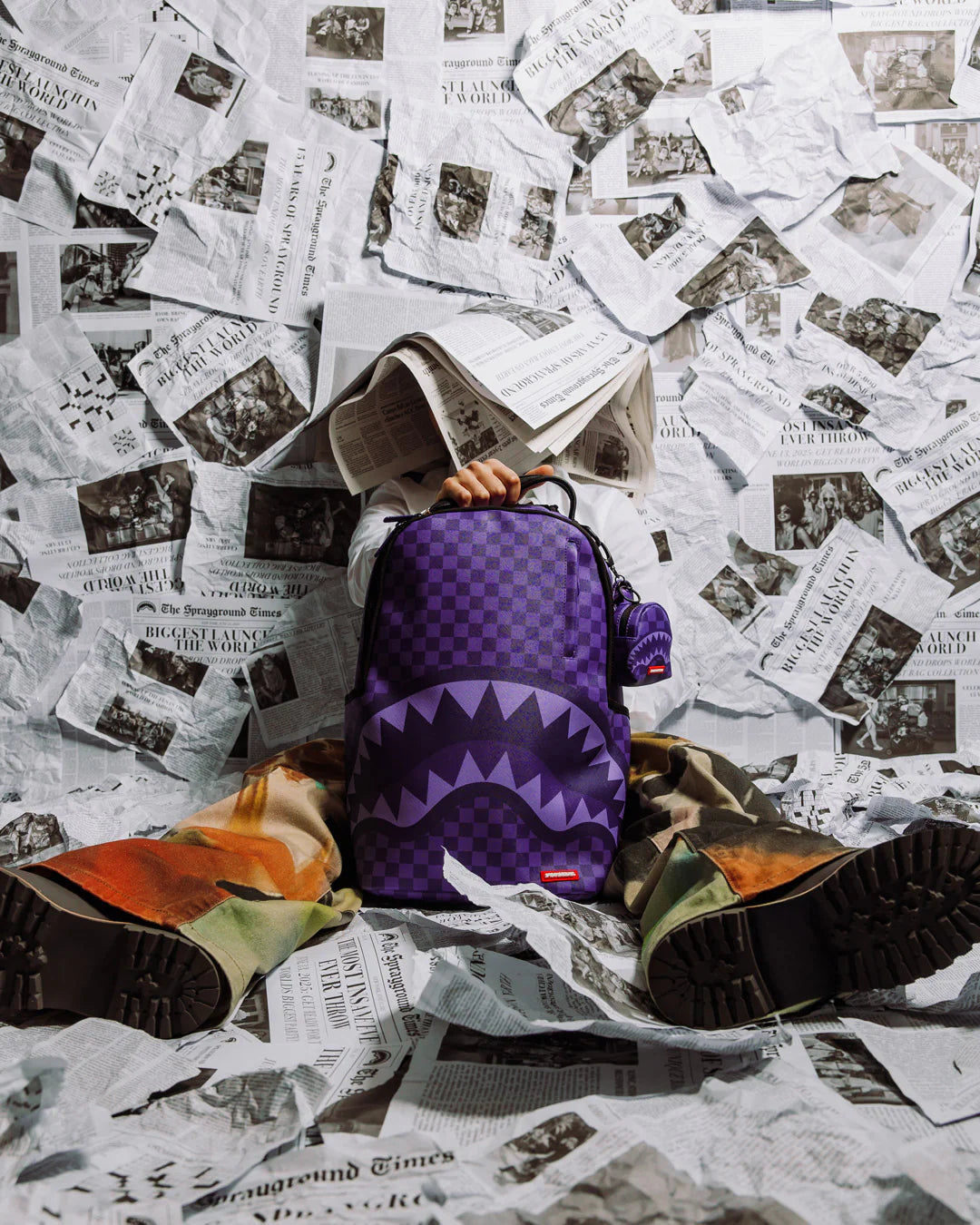 Purple checkered backpack with shark mouth design on a white background by sprayground