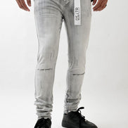 Person wearing light gray distressed jeans with a brand label on a white background