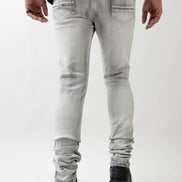 Person wearing light gray jeans and black shoes on a white background