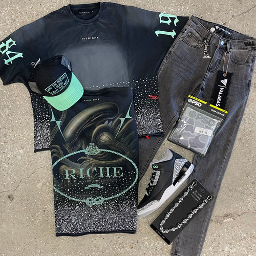 Fashion items including a t-shirt, jeans, sneakers, and accessories on a concrete surface.