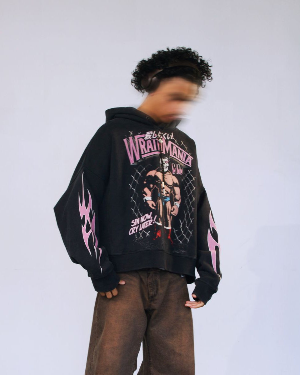 Person wearing a black hoodie with graphic designs and text on a plain background